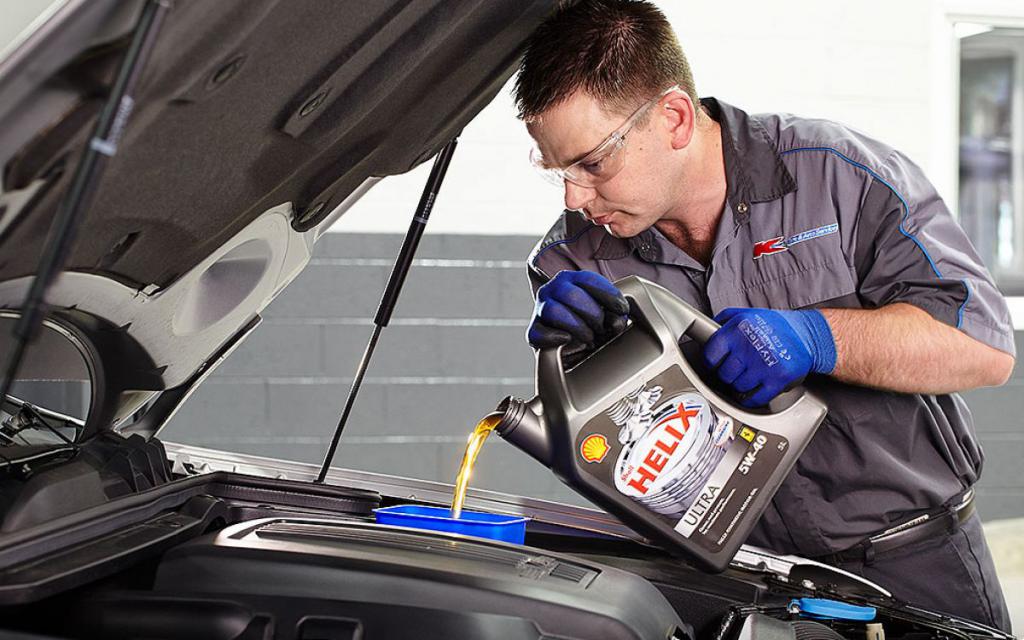 Механик заливает масло в двигатель.